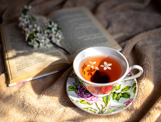 mug of tea, black tea in a mug, a sprig of blossoming, a shadow, on a plaid stands a mug of tea,