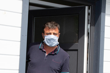Fototapeta na wymiar man with face protect mask looking worried at front home door in case visitors bring coronavirus to house