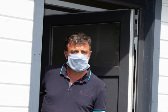 Man With Face Protect Mask Looking Worried At Front Home Door In Case Visitors Bring Coronavirus To House