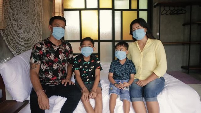 Asian family in medical masks during home quarantine. Indonesian or malasian parents and kids wearing protective mask at home during coronavirus covid-19 outbreak