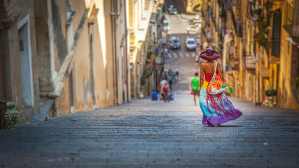Tanned young woman, with multicolored dress and hat, goes down the staircase of Caltagirone in Sicily