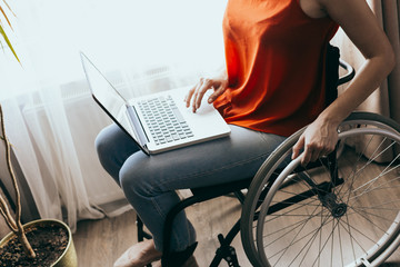 Woman in a wheelchair at home with a laptop on her lap, hand close up, unrecognizable man.