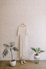 simple white wedding dress hanging on a white brick wall