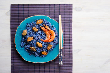 Blue rice with shrimp and mussels on a blue plate on a purple mat, white background. Seafood