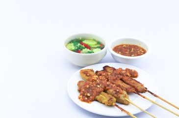 pork satay served on white round dish on white background and there is copy space. Also peanut sauce and cucumber release served along side.