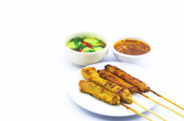 pork satay served on white round dish on white background and there is copy space. Also peanut sauce and cucumber release served along side.