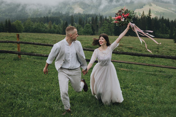 Spring wedding in the mountains. A guy in a shirt and vest and a girl in a white dress walk along a...