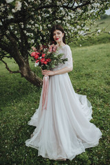 Spring wedding in the mountains. A young girl in a white dress stands near a blossoming tree in the...