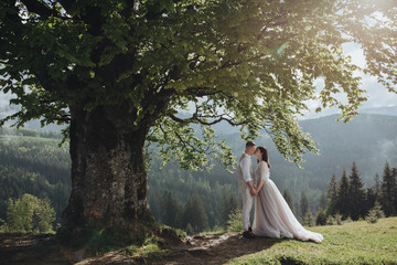 Spring wedding in the mountains. A young guy in a white shirt and trousers and a girl in a white...