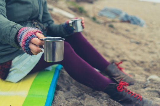 Young woman with two cups of tea on the beach in winter