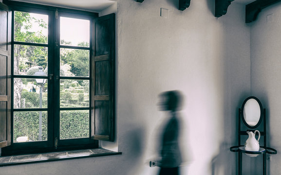 Silueta borrosa de una mujer mirando con melancol&iacute;a al exterior por una ventana con ganas de poder salir del confinamiento y no tener que quedarse en casa