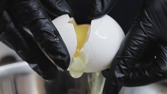 Female hands break an egg into a plate. Female hands in black gloves. Cooking