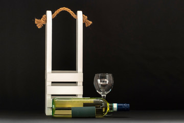 white wine bottle, decorative wooden packaging and a glass on a black background