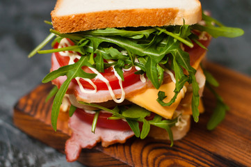 Huge delicious sandwich with ham and sturgeon, arugula, cheese, tomato and mayonnaise on a cutting...
