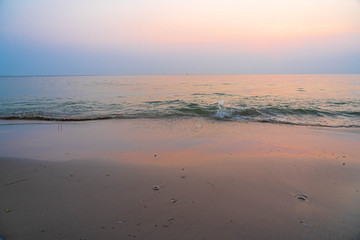 The golden light from the morning sun reflects on the sea and the waves that hit the sand on the beach.