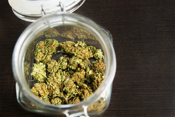 Cannabis buds in glass jar closeup on wooden background.