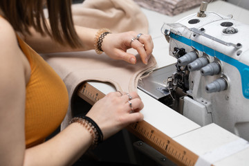 A teenager sews a brown dress on a sewing machine called an overlock.