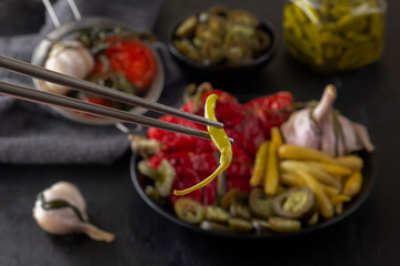 Chopsticks contain fermented green hot peppers on the background of pickled food. Close-up
