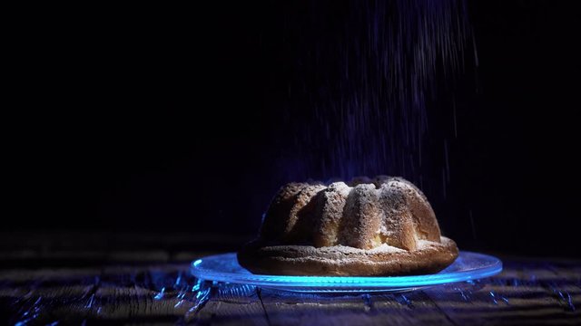 Babka - Ciasto na stole ( deska ) . Ciemne tło . Cukier puder .  Posypywanie cukrem pudrem. 