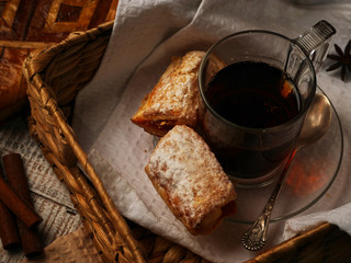 Tea with sweet cookies in a wicker tray on white wooden background. Cinnamon stiks lay near the afteroon tea