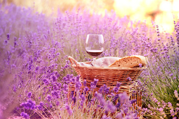 Wine against lavender landscape in sunset rays. Harvesting of aromatic lavender. A basket filled with fresh bread stands at midlle of lavender field.