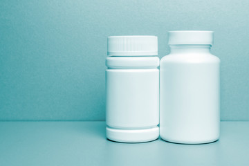 2 white jars for medicines and vitamins and dietary supplements without a name are on a gray shelf. copy space to the left. layout for a pharmacy, a store. blue tinted