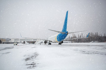 Passenger plane at airport in winter in blizzard. Landing passengers in airliner in winter during snowstorm. Modern twin-engine passenger airplane at airport during snow blizzard