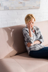 Tired mature woman with headache sitting on sofa in living room