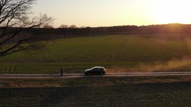 Schwarzes Auto SUV auf Feldweg voller Staub beim Sonnenuntergang f&auml;hrt auf Person zu w&auml;hrend der Corona Pandemie