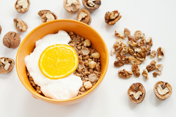Muesli, granola with yogurt and orange in yellow bowl on white background with walnuts