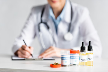 selective focus of dried marijuana, bottles with cbd and medical cannabis lettering near doctor writing prescription - obrazy, fototapety, plakaty