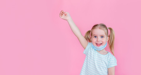 Optimistic, smiling happy little girl taking off the medical mask from face on a pink background with hand up showing end of the pandemia. Copyspace.