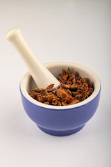 star anise in a blue ceramic spice mortar with a pestle on a white background. Close up.