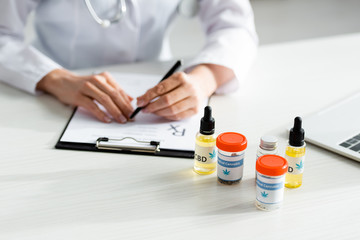selective focus of bottles with medical cannabis and cbd near doctor writing prescription