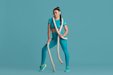 Confidence. Beautiful young female athlete practicing in studio, monochrome blue portrait. Sportive fit brunette model with ropes. Body building, healthy lifestyle, beauty and action concept.
