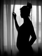 Silhouette of pregnant woman standing by window in bedroom.
