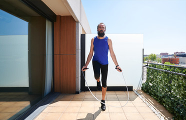 front view of a man in sportswear jumping rope on the terrace of his house