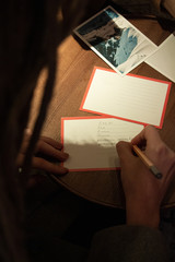 The girl writes a letter in pencil on a card that lies on the table