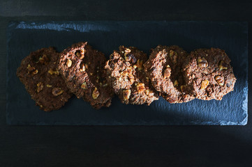homemade cookies of oats, chocolate and nuts on blackboard bathed in a strip of sunlight