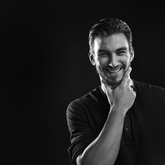 Fototapeta na wymiar Black and white portrait of a courageous attractive laughing man holding a hand near his face isolated on a black background.