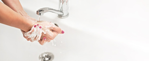 Young woman washing her hands under water tap faucet with soap, nails covered purple polish. Wide...