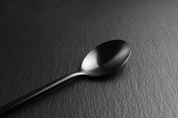 A black matte spoon rests on a black slate. Close up.