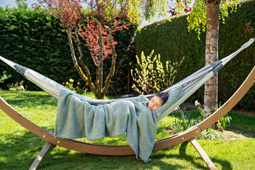 Young relaxed girl sleeping peacefully in hammock in garden at home at bright sunny day. Slow living, gadget detox and weekend leisure activity. Quarantine and self isolation period