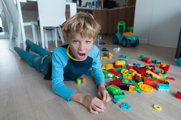 sad young boy shouting with toys scattered around, child in stress