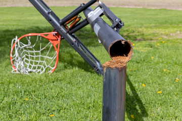 Outdoor basketball hoop with in-ground pole rusty and broken from dunking and wind damage