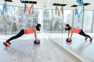 Woman making exercises with ball before mirror in gym