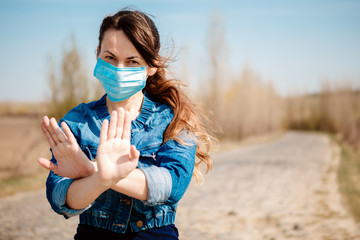 Woman in protective sterile medical mask on her face looking at camera outdoors. Hand stop Sign . Pandemic coronavirus concept.