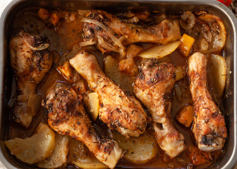 Roasted Chicken legs on metal baking tray with potatoes, onion. tomatoes witn spices. Top view.
