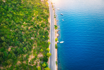 Aerial view of road in beautiful green forest and boats in the sea at sunset in summer. Colorful...