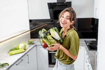Portrait of a young and cheerful woman with healthy raw food on the kitchen at home. Vegetarianism, wellbeing and healthy lifestyle concept